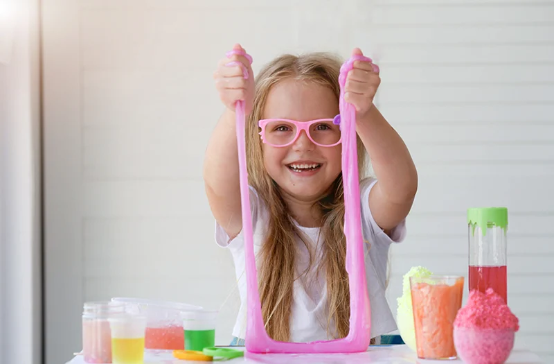 Een lachend meisje met roze bril speelt met roze slijm tijdens een wetenschappelijk experiment.